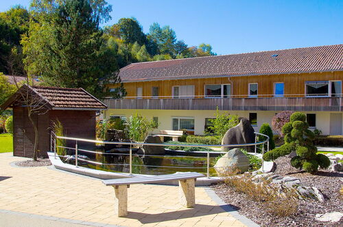 Garten mit Teich, kleiner Holzbrücke, Steinskulptur und zweistöckigem Gebäude im Hintergrund